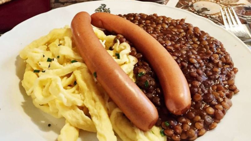 Ein Teller mit Linsen, Spätzle und zwei Würstchen, serviert auf einem Tisch mit Besteck., © TMBW, Susi Maier