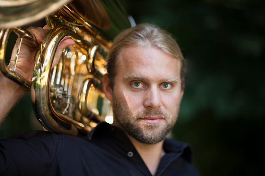 Ein Mann mit blonden Haaren tr&auml;gt eine Tuba auf der Schulter und blickt ernst in die Kamera. Der Hintergrund ist unscharf und dunkel., &copy; Philippe Gerlach