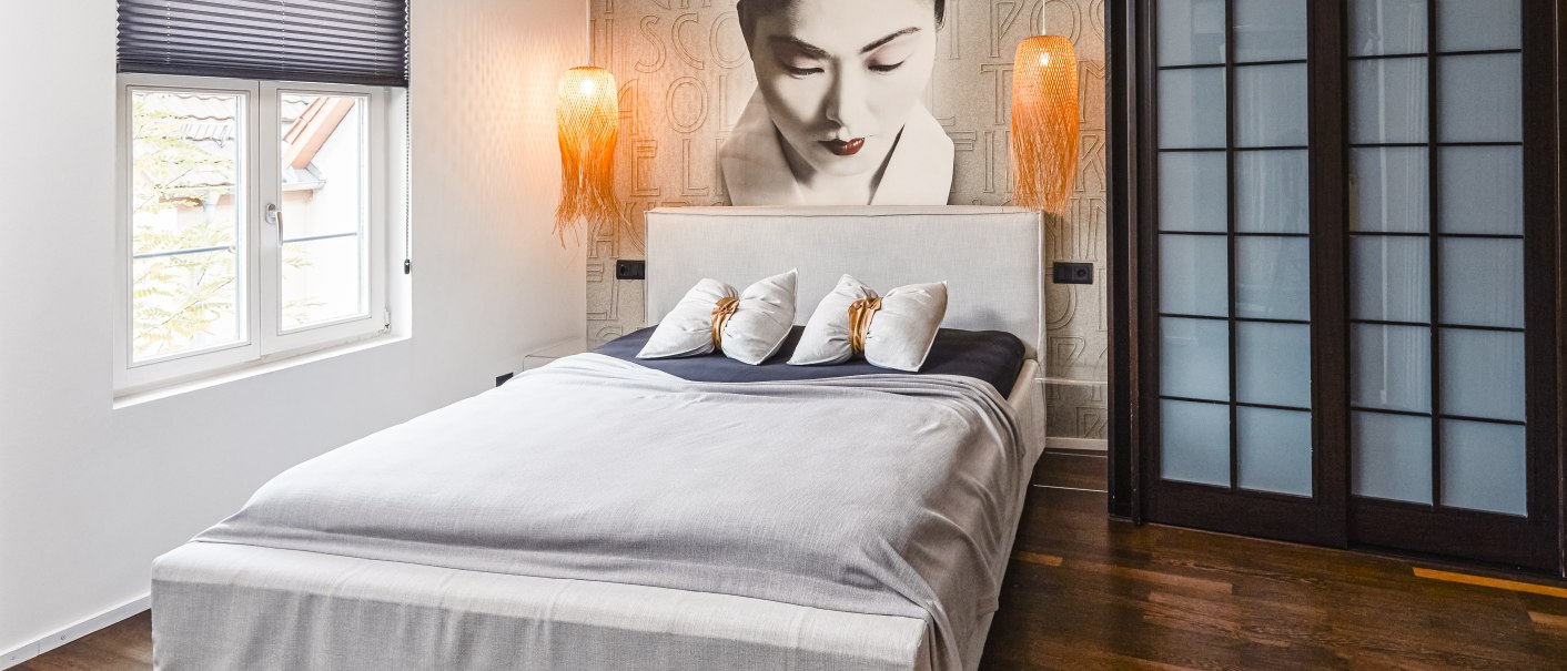 Modernes Hotelzimmer mit großem Bett, Wandbild einer Frau, zwei Hängelampen und Holzfußboden., © Zauberlehrling Modernes Hotelzimmer mit großem Bett, Wandbild einer Frau, zwei Hängelampen und Holzfußboden., © Zauberlehrling