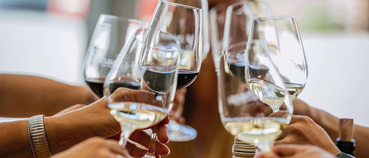 Several hands hold wine glasses and clink glasses. The glasses contain red and white wine. Cheerful atmosphere on a wine tour., © SMG, Thomas Niedermüller