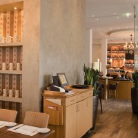Stylish restaurant with wooden furniture, shelves full of cups and a cozy atmosphere. Guests sit at tables, with a bar in the background., &copy; Aspectus Photographie Stuttgart