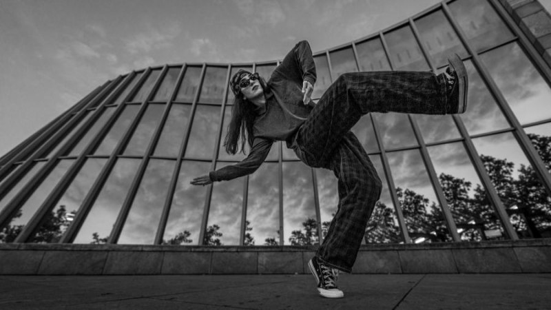 Frau tanzt in dynamischer Pose vor einem modernen Gebäude mit Glasfassade. Schwarz-weiß-Fotografie, dramatische Perspektive., © Fotocredit Theater La Lune Stuttgart