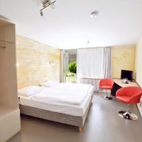 Helles Zimmer mit Doppelbett, zwei roten Stühlen, Schreibtisch, Fernseher und großem Fenster mit Blick ins Grüne., © Abalon Hotel Ideal Helles Zimmer mit Doppelbett, zwei roten Stühlen, Schreibtisch, Fernseher und großem Fenster mit Blick ins Grüne., © Abalon Hotel Ideal