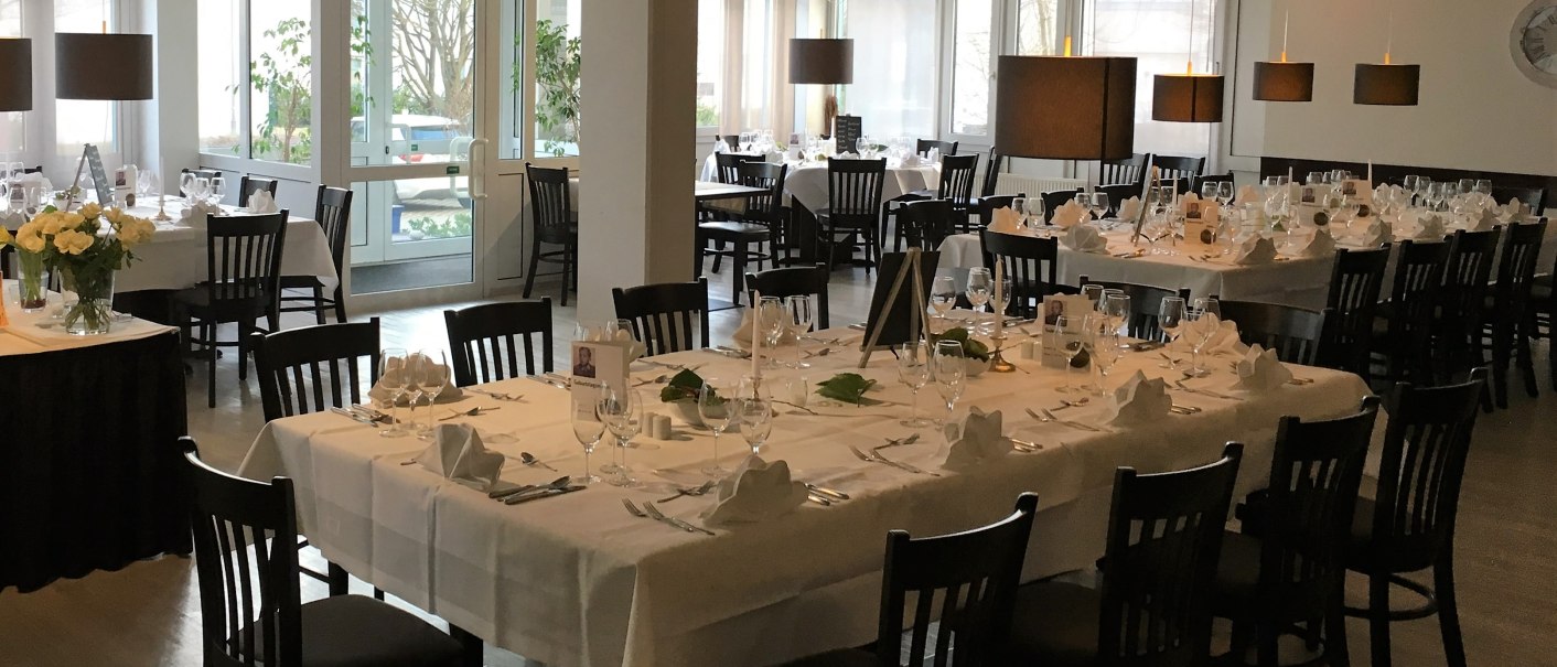An elegant restaurant with tables set with white linens, black chairs, and decorative lamps. The tables are set up for an event., &copy; bonjour Hotelbetriebs GmbH