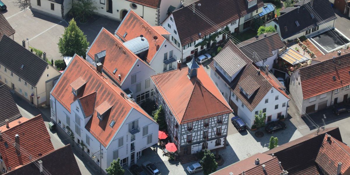 Luftaufnahme eines Dorfes mit Fachwerkhäusern und roten Dächern. Im Zentrum ein Gebäude mit rotem Dach und Sonnenschirmen., © Hotel Gasthof Lamm