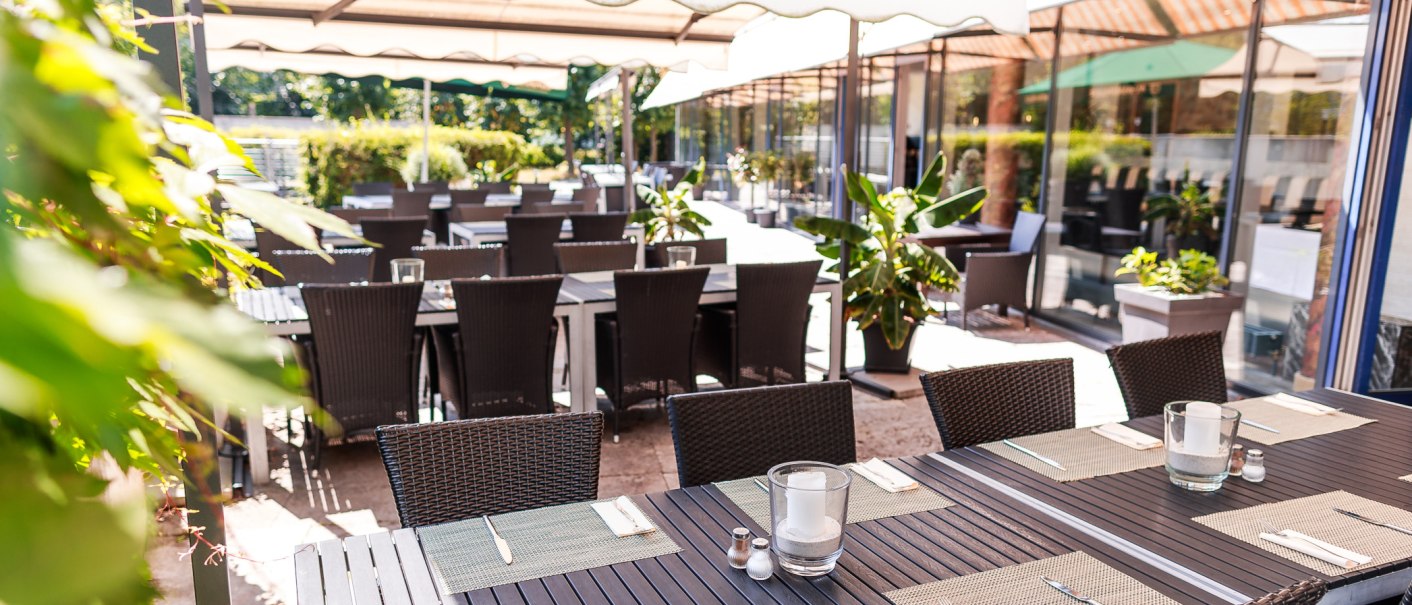 Restaurant terrace with covered tables and chairs under parasols, surrounded by plants., © PLAZA Hotelgroup GmbH