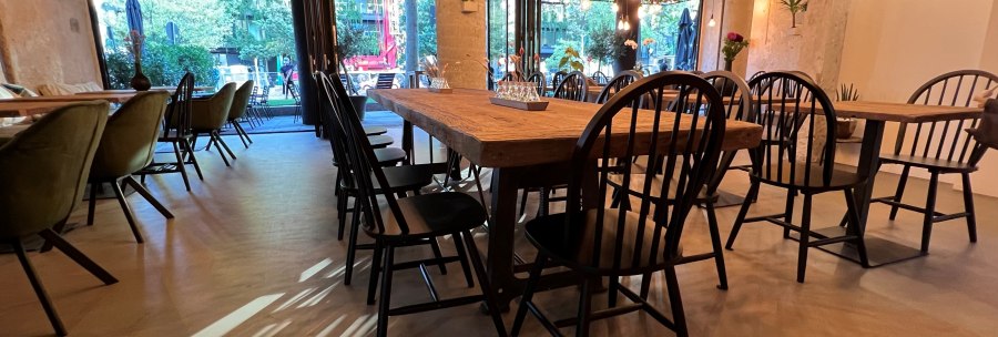 Ein stilvoll eingerichtetes Restaurant mit Holztischen, schwarzen Stühlen und einer Decke voller Lichterketten., © heavenskitchen Ein stilvoll eingerichtetes Restaurant mit Holztischen, schwarzen Stühlen und einer Decke voller Lichterketten., © heavenskitchen