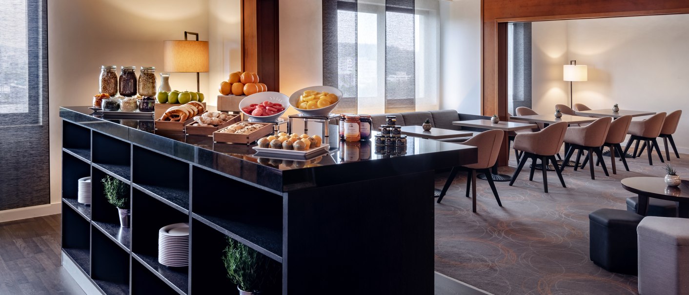 Modern lounge with breakfast buffet offering fruit, pastries and jams. Tables and chairs in an elegant room can be seen in the background., © Stuttgart Marriott Hotel Sindelfingen Modern lounge with breakfast buffet offering fruit, pastries and jams. Tables and chairs in an elegant room can be seen in the background., © Stuttgart Marriott Hotel Sindelfingen