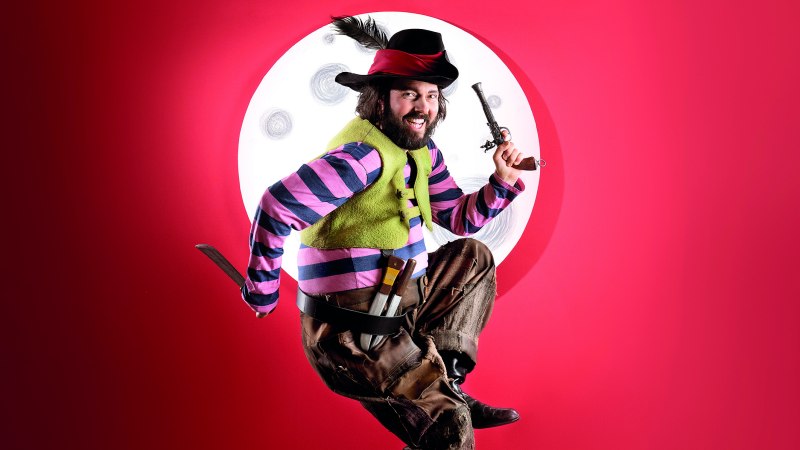 Person in bunter Piratenkleidung springt vor einem roten Hintergrund mit einem Mond im Hintergrund. Sie hält eine Pistole und ein Messer., © Martin Sigmund Person in bunter Piratenkleidung springt vor einem roten Hintergrund mit einem Mond im Hintergrund. Sie hält eine Pistole und ein Messer., © Martin Sigmund