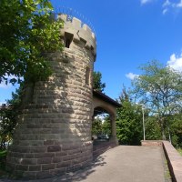 Runder Steinturm mit Zinnen, umgeben von Bäumen und blauem Himmel. Der Turm steht auf einer gepflasterten Fläche., © SMG