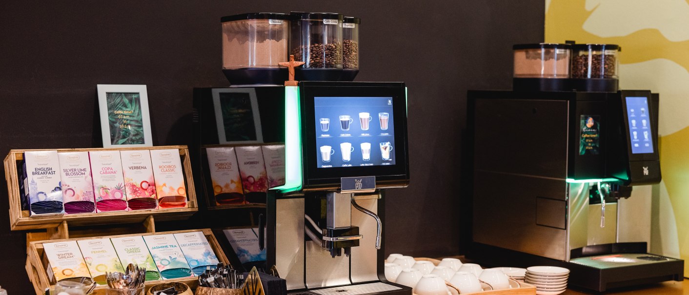 Two coffee machines with touch screen, tea assortment and pastries on a table. Cups and spoons are provided., © Rioca Stuttgart Posto 4 GmbH Two coffee machines with touch screen, tea assortment and pastries on a table. Cups and spoons are provided., © Rioca Stuttgart Posto 4 GmbH
