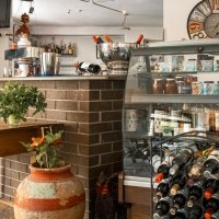 Gem&uuml;tliches Caf&eacute; mit Holztisch, Weinregal, dekorativen Bildern und Pflanzen. Eine Theke mit Getr&auml;nken und ein Fernseher sind ebenfalls zu sehen., &copy; SMG, Sarah Schmid