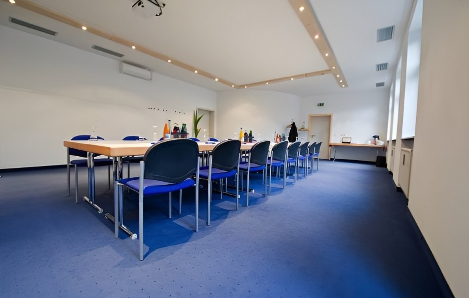 Empty conference room with a large table, blue chairs and blue carpeting. Drinks and a projector can be seen on the wall., © Hotel Neuwirtshaus Empty conference room with a large table, blue chairs and blue carpeting. Drinks and a projector can be seen on the wall., © Hotel Neuwirtshaus