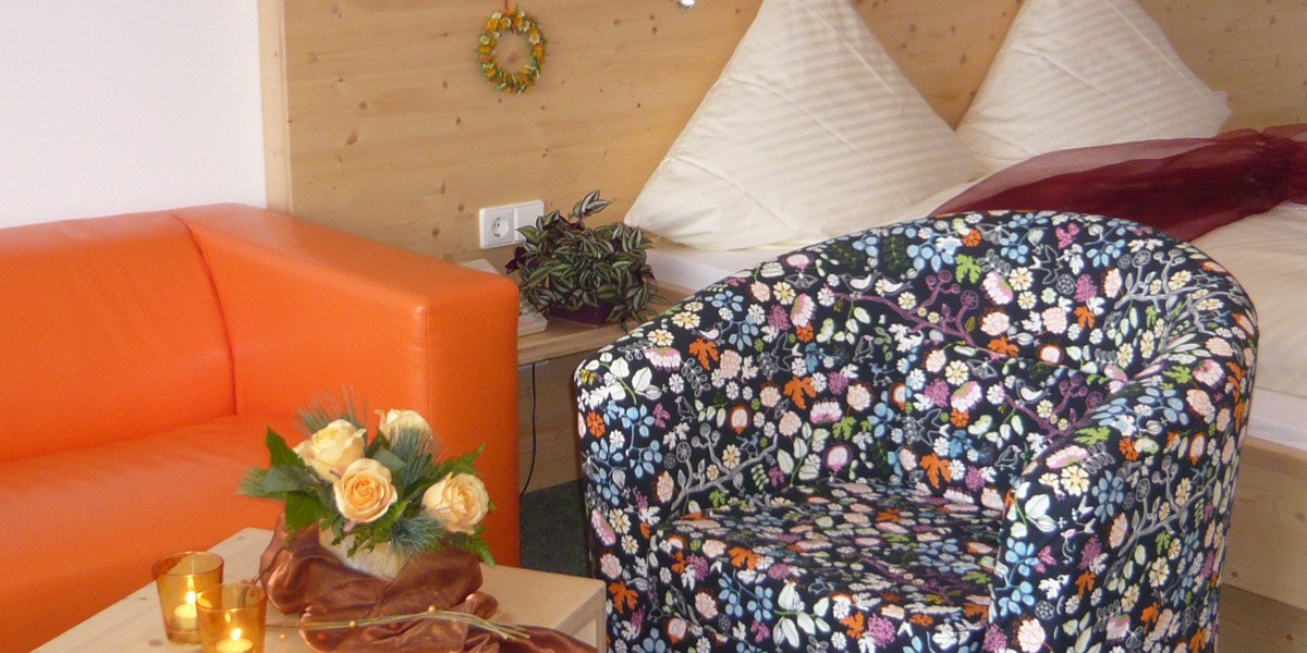 Cozy double room with orange couch, floral armchair, bouquet of flowers and bed in the background., &copy; Hotel Hochwald