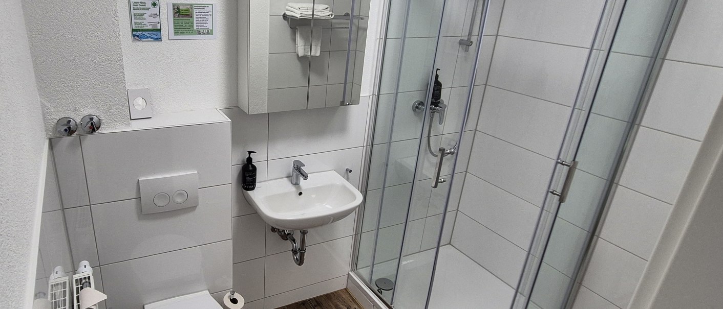 Modernes Badezimmer mit Dusche, Waschbecken, Spiegel, Toilette und Handtuchhalter. Wei&szlig;e Fliesen und Holzboden sorgen f&uuml;r ein sauberes Ambiente., &copy; MedientechnikKeuk