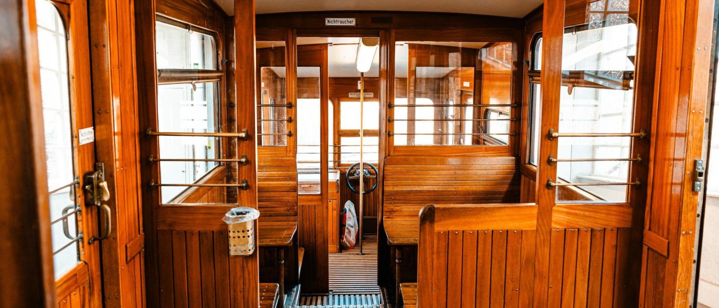 Innenansicht einer historischen Seilbahnkabine aus Holz mit Sitzbänken, Lenkrad und "Nichtraucher"-Schild. Die Kabine hat große Fenster., © Stuttgart Marketing GmbH, Sarah Schmid