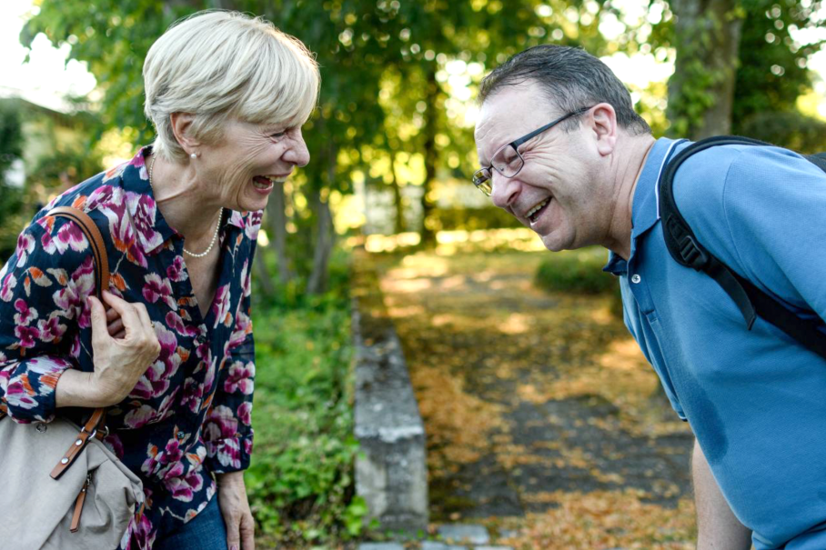 Zwei Personen, eine Frau und ein Mann, lachen herzlich im Freien. Die Frau trägt eine bunte Bluse, der Mann ein blaues Polohemd., © Weltkino Zwei Personen, eine Frau und ein Mann, lachen herzlich im Freien. Die Frau trägt eine bunte Bluse, der Mann ein blaues Polohemd., © Weltkino