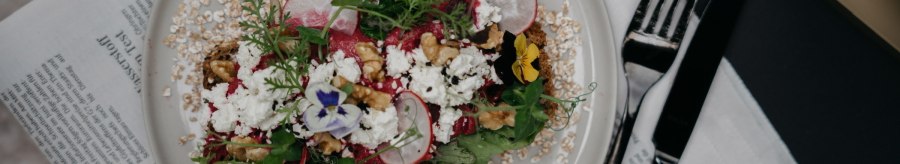 A decorative salad with radishes, nuts and edible flowers on a plate, served on a newspaper., © Fritz, Stuttgart