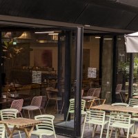 Outdoor area of a café with wooden tables and green chairs. An awning bears the lettering 'Citizen Long'. Plants decorate the area., © SMG, Sarah Schmid Outdoor area of a café with wooden tables and green chairs. An awning bears the lettering 'Citizen Long'. Plants decorate the area., © SMG, Sarah Schmid