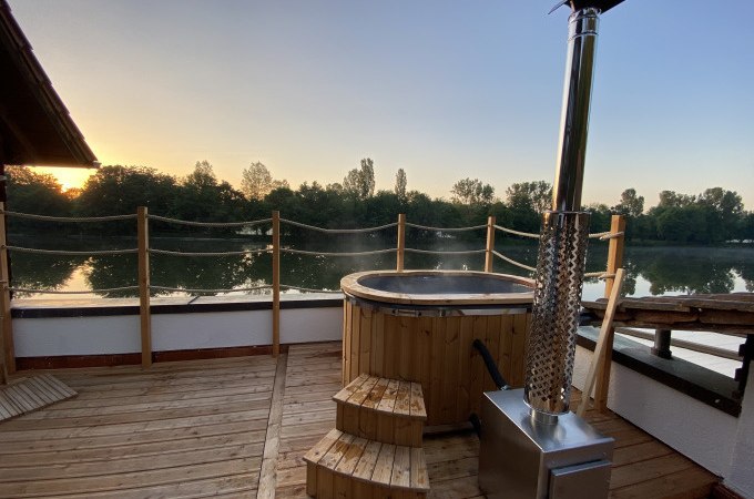 Holzterrasse mit Hot Tub, daneben ein Ofen. Im Hintergrund ein Fluss und B&auml;ume bei Sonnenuntergang., &copy; Cool-Tours StattReisen