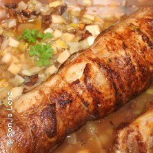 Gebratenes Fleischstück in einer Pfanne mit Gemüse und Kräutern, dekoriert mit Petersilie., © links im Bild