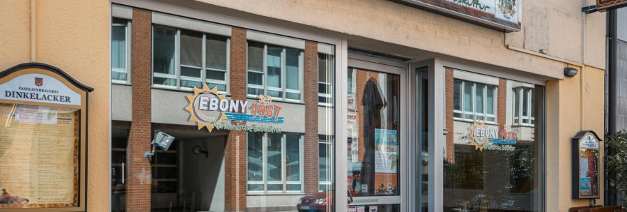 Eingang des Restaurants 'Ebony' mit Schildern f&uuml;r afrikanische K&uuml;che. Fenster spiegeln die gegen&uuml;berliegende Stra&szlig;e wider. Seit 1987 ge&ouml;ffnet., &copy; SMG, Sarah Schmid