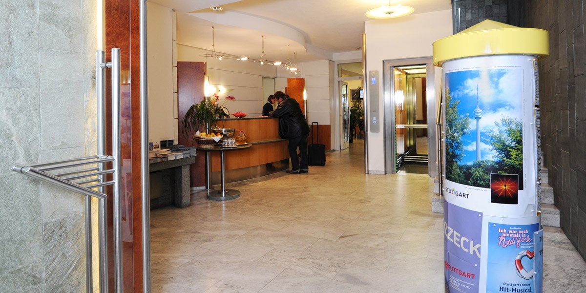 Hotelrezeption mit Personen am Empfangstresen, Aufzug im Hintergrund, Werbesäule mit Stuttgart-Motiv im Vordergrund., © Hotel Unger