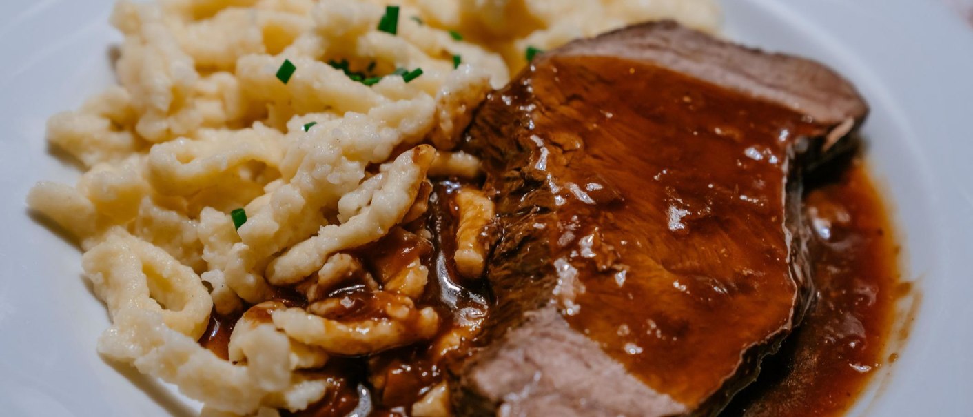 A plate of succulent roast in a dark sauce, served with spaetzle and garnished with chives., © SMG, Thomas Niedermüller