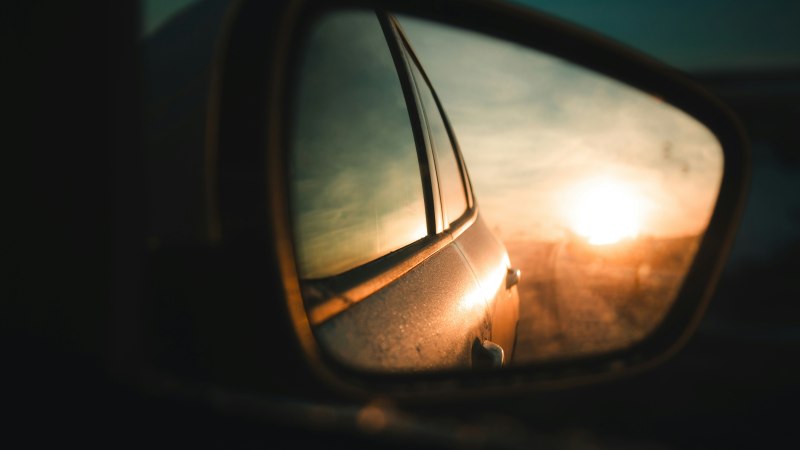 Ein Auto-Rückspiegel zeigt die untergehende Sonne und die Straße im Hintergrund. Die Szene vermittelt eine nostalgische Stimmung., © Stan Jabocs / unsplah Ein Auto-Rückspiegel zeigt die untergehende Sonne und die Straße im Hintergrund. Die Szene vermittelt eine nostalgische Stimmung., © Stan Jabocs / unsplah