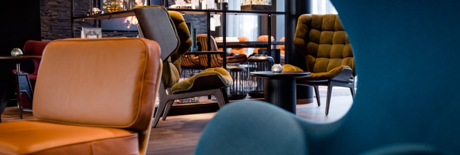 Moderne Lounge mit stilvollen Sesseln in Blau und Braun, Regalen mit Dekorationen und gemütlicher Atmosphäre., © TOMAS Moderne Lounge mit stilvollen Sesseln in Blau und Braun, Regalen mit Dekorationen und gemütlicher Atmosphäre., © TOMAS