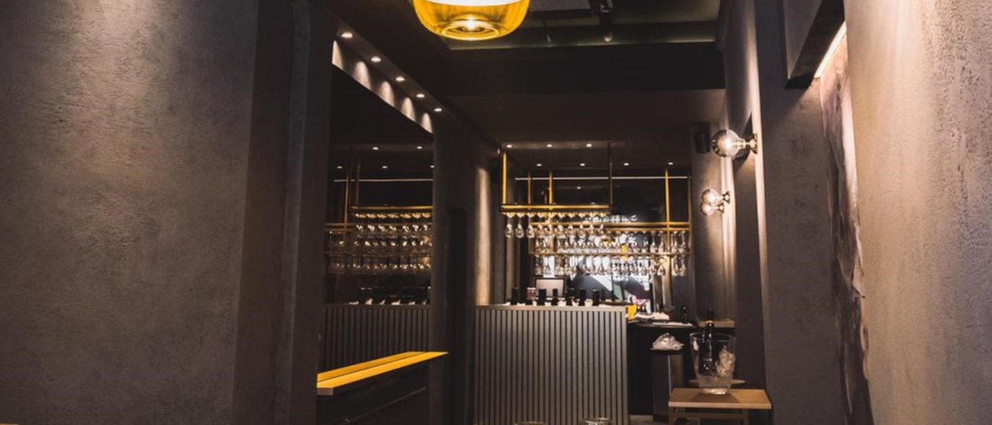 Stilvolle Bar mit modernem Design, hängenden Gläsern und eleganter Beleuchtung. Der Tresen ist zentral platziert, umgeben von dunklen Wänden., © KESSLER Sekt GmbH & Co. KG