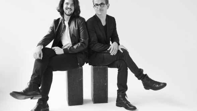 Two men sit smiling on blocks in a studio. Black and white photograph with plain background., © Internationale Hugo-Wolf-Akademie Two men sit smiling on blocks in a studio. Black and white photograph with plain background., © Internationale Hugo-Wolf-Akademie