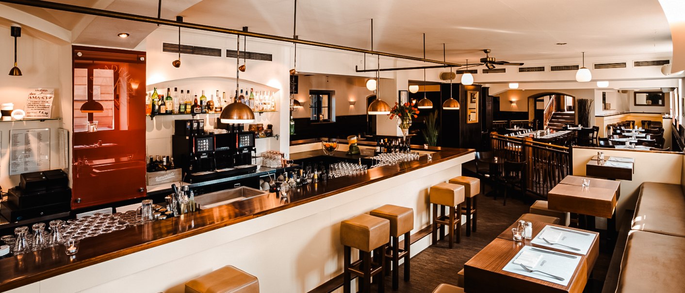 A stylish restaurant with a bar, wooden furniture and modern lighting. The bar is well stocked and there is seating with covered tables., © Amadeus A stylish restaurant with a bar, wooden furniture and modern lighting. The bar is well stocked and there is seating with covered tables., © Amadeus