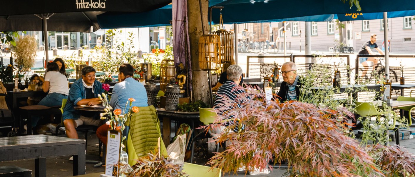 Ein belebtes Café im Freien mit Menschen, die an Tischen unter Sonnenschirmen sitzen. Pflanzen und Dekorationen schaffen eine gemütliche Atmosphäre., © SMG Stuttgart Marketing GmbH - Sarah Schmid