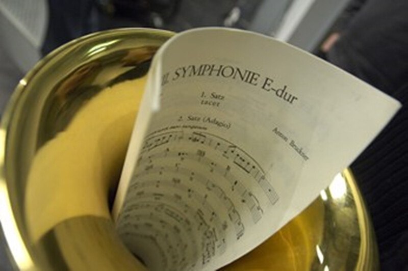 A sheet of music for Anton Bruckner's Symphony in E-Major is tucked inside a horn. The focus is on the score and the instrument., © Württembergische Staatstheater Stuttgart A sheet of music for Anton Bruckner's Symphony in E-Major is tucked inside a horn. The focus is on the score and the instrument., © Württembergische Staatstheater Stuttgart