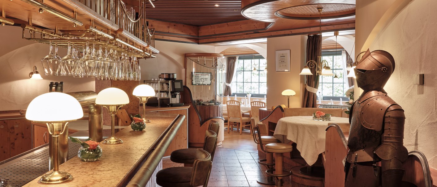 A rustic bar area at the Badhotel Restaurant Stauferland, featuring a wooden ceiling, bar stools, a suit of armor, and cozy lighting., © Badhotel Restaurant Stauferland A rustic bar area at the Badhotel Restaurant Stauferland, featuring a wooden ceiling, bar stools, a suit of armor, and cozy lighting., © Badhotel Restaurant Stauferland