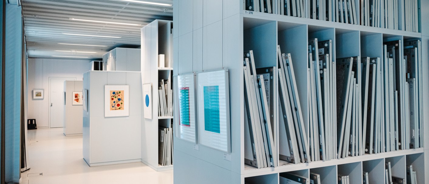 Interior view of a modern art library with shelves full of framed works of art and light-colored walls. Pictures hang on the walls., © Sarah Schmid Interior view of a modern art library with shelves full of framed works of art and light-colored walls. Pictures hang on the walls., © Sarah Schmid