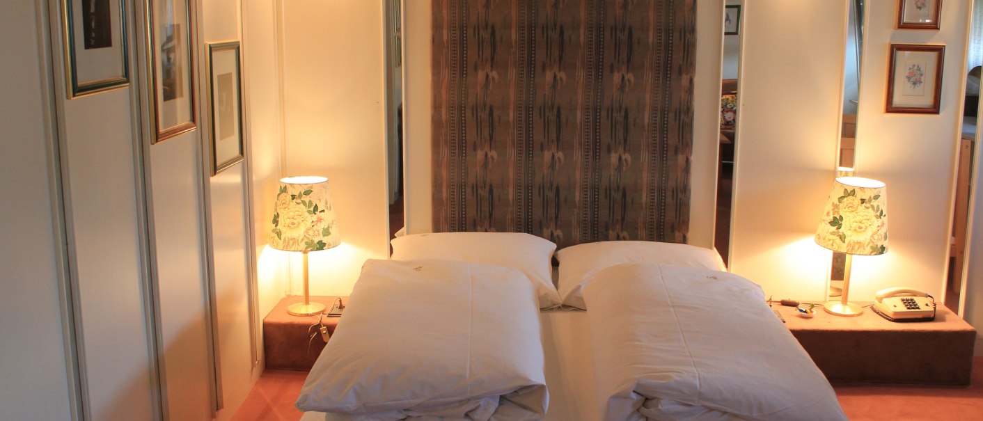 A cozy hotel room with a double bed, two bedside lamps, and decorative pictures on the wall., &copy; Hotel Spahr