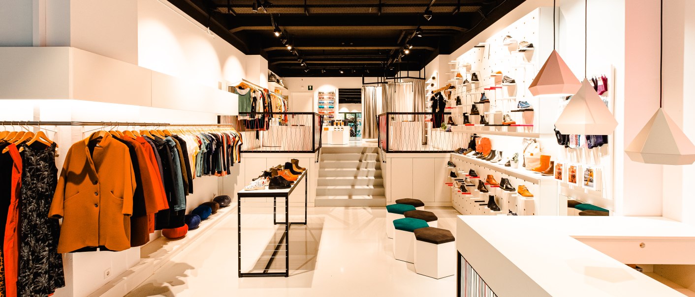 Ein modernes Bekleidungsgeschäft mit stilvoller Einrichtung, Kleidung an Kleiderstangen und Schuhen auf Regalen. Helle Beleuchtung und geometrische Lampen., © Elisa Mauruschat Ein modernes Bekleidungsgeschäft mit stilvoller Einrichtung, Kleidung an Kleiderstangen und Schuhen auf Regalen. Helle Beleuchtung und geometrische Lampen., © Elisa Mauruschat