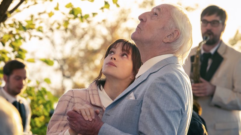 Ein älterer Mann und eine junge Frau schauen gemeinsam in den Himmel, während ein Musiker im Hintergrund ein Saxophon spielt., © Filmwelt Verleihagentur