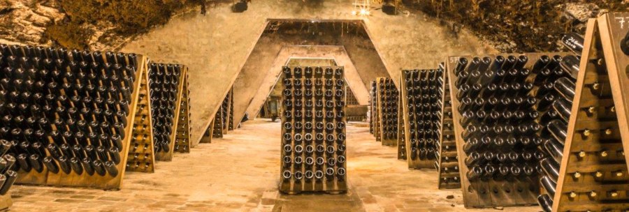 Ein Gewölbekeller im Kessler Sektkeller mit zahlreichen Sektflaschen, die in Holzgestellen lagern. Die Atmosphäre ist warm und rustikal., © KESSLER Sekt GmbH & Co. KG