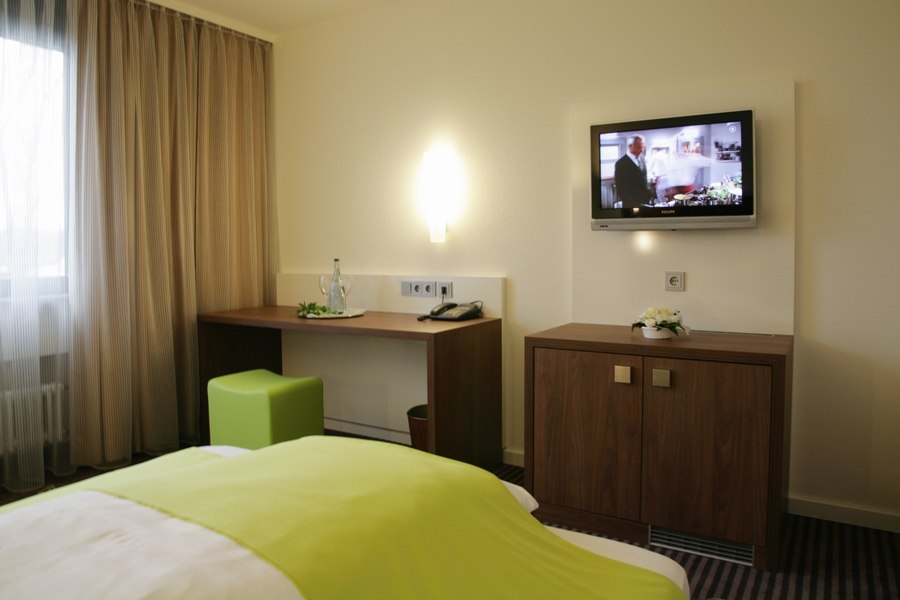 A modern single room with a green bedspread, desk, TV on the wall and a window with curtains., © Hotel Fuchsen A modern single room with a green bedspread, desk, TV on the wall and a window with curtains., © Hotel Fuchsen