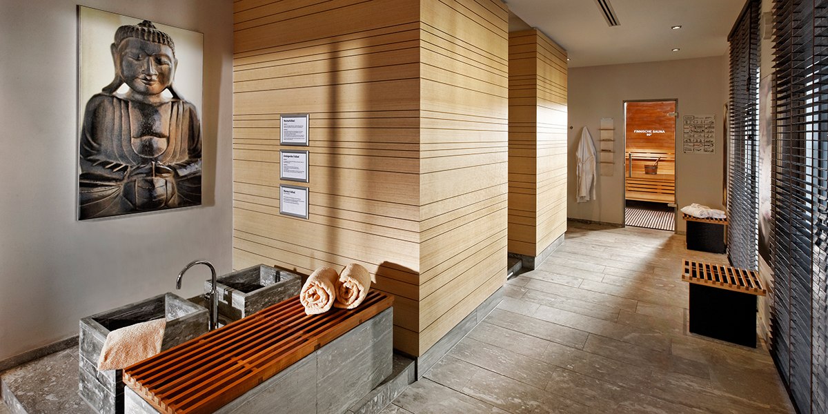 Ein Spa-Bereich mit Buddha-Bild, Holzverkleidung, Handtüchern und einer Sauna im Hintergrund., © Parkhotel Stuttgart Messe-Airport Ein Spa-Bereich mit Buddha-Bild, Holzverkleidung, Handtüchern und einer Sauna im Hintergrund., © Parkhotel Stuttgart Messe-Airport