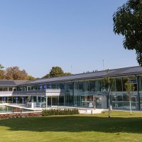 The picture shows the outdoor area of the Mineralbad Berg with a pool, surrounded by modern buildings and green trees under a clear sky., © Stuttgarter Bäder