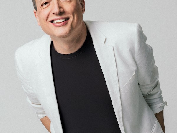 Eine l&auml;chelnde Person in einem wei&szlig;en Anzug und schwarzem T-Shirt vor einem neutralen Hintergrund., &copy; Rosenau Kultur e.V.