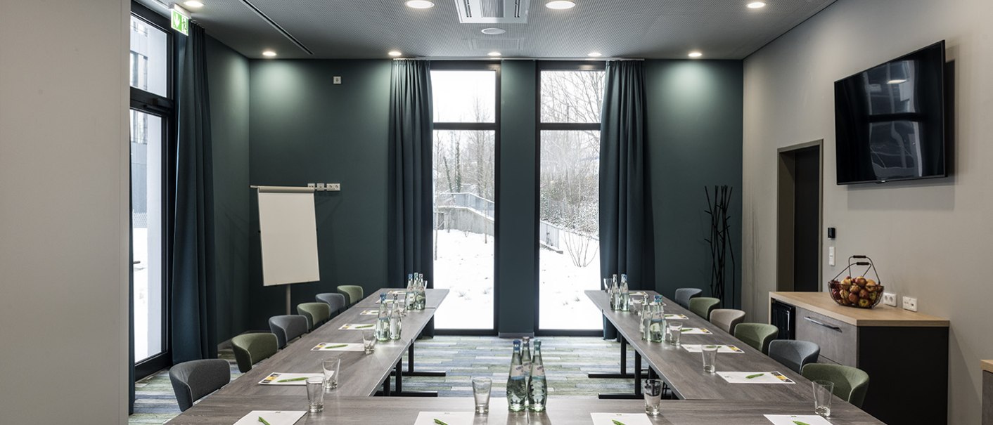 Moderner Konferenzraum mit U-förmigem Tisch, Flipchart, großem Fenster und TV. Wasserflaschen und Notizblöcke auf den Tischen, Obstkorb auf der Anrichte., © ibis Styles Stuttgart Vaihingen Moderner Konferenzraum mit U-förmigem Tisch, Flipchart, großem Fenster und TV. Wasserflaschen und Notizblöcke auf den Tischen, Obstkorb auf der Anrichte., © ibis Styles Stuttgart Vaihingen