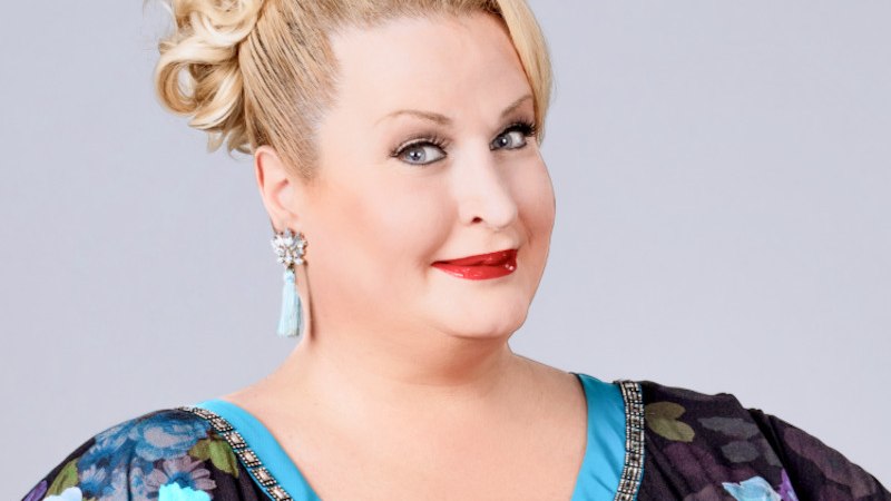 Eine Frau mit blonden Locken und floralem Kleid lächelt in die Kamera. Sie trägt auffällige Ohrringe und roten Lippenstift., © Renitenztheater Eine Frau mit blonden Locken und floralem Kleid lächelt in die Kamera. Sie trägt auffällige Ohrringe und roten Lippenstift., © Renitenztheater