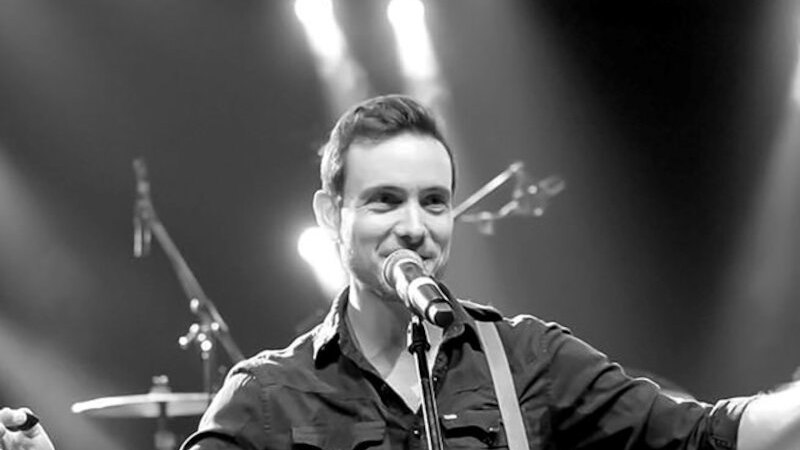 Ein Musiker steht auf der Bühne, singt ins Mikrofon und spielt Gitarre. Im Hintergrund sind Schlagzeug und Scheinwerfer zu sehen., © Theaterhaus Stuttgart e.V. Ein Musiker steht auf der Bühne, singt ins Mikrofon und spielt Gitarre. Im Hintergrund sind Schlagzeug und Scheinwerfer zu sehen., © Theaterhaus Stuttgart e.V.