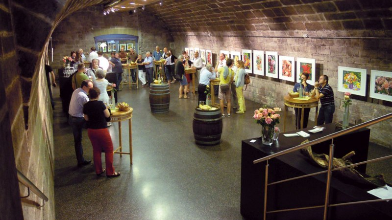 Menschen in einem Gewölbekeller betrachten Kunstwerke an den Wänden. Tische und Weinfässer dienen als Stehtische. Blumen schmücken den Raum., © Collegium Wirtemberg Menschen in einem Gewölbekeller betrachten Kunstwerke an den Wänden. Tische und Weinfässer dienen als Stehtische. Blumen schmücken den Raum., © Collegium Wirtemberg