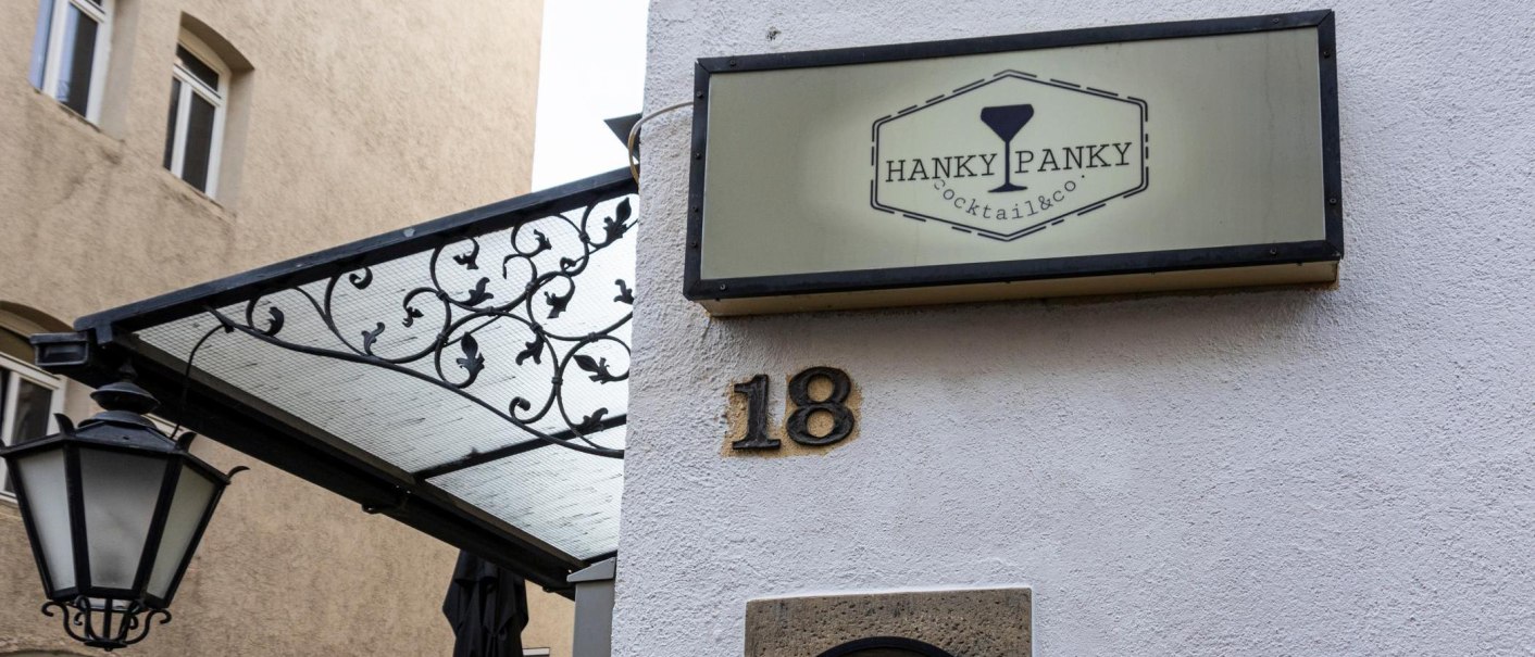 A sign reading 'Hanky Panky Cocktail & co' hangs on a wall next to house number 18. A lantern and a decorative canopy are visible., © Stuttgart-Marketing GmbH, Sarah Schmid A sign reading 'Hanky Panky Cocktail & co' hangs on a wall next to house number 18. A lantern and a decorative canopy are visible., © Stuttgart-Marketing GmbH, Sarah Schmid